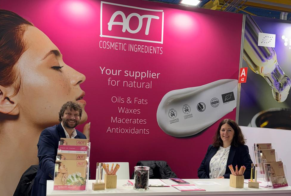 AOT-Messestand auf der Cosmoprof 2026 mit Team vor pinker Rückwand „Your supplier for natural ingredients“