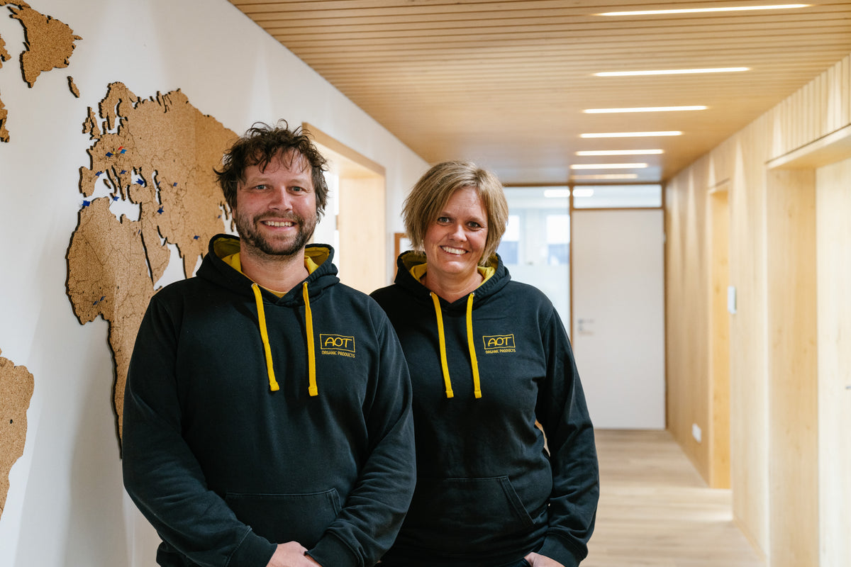 Zwei AOT-Mitarbeitende in Firmen-Hoodies im Flur vor einer Weltkarte